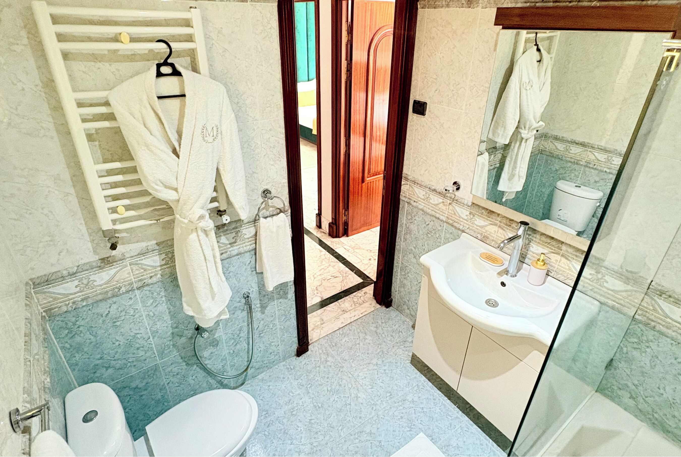 A bathroom with a white sink, a toilet, a glass shower enclosure, and a robe hanging on a rack.