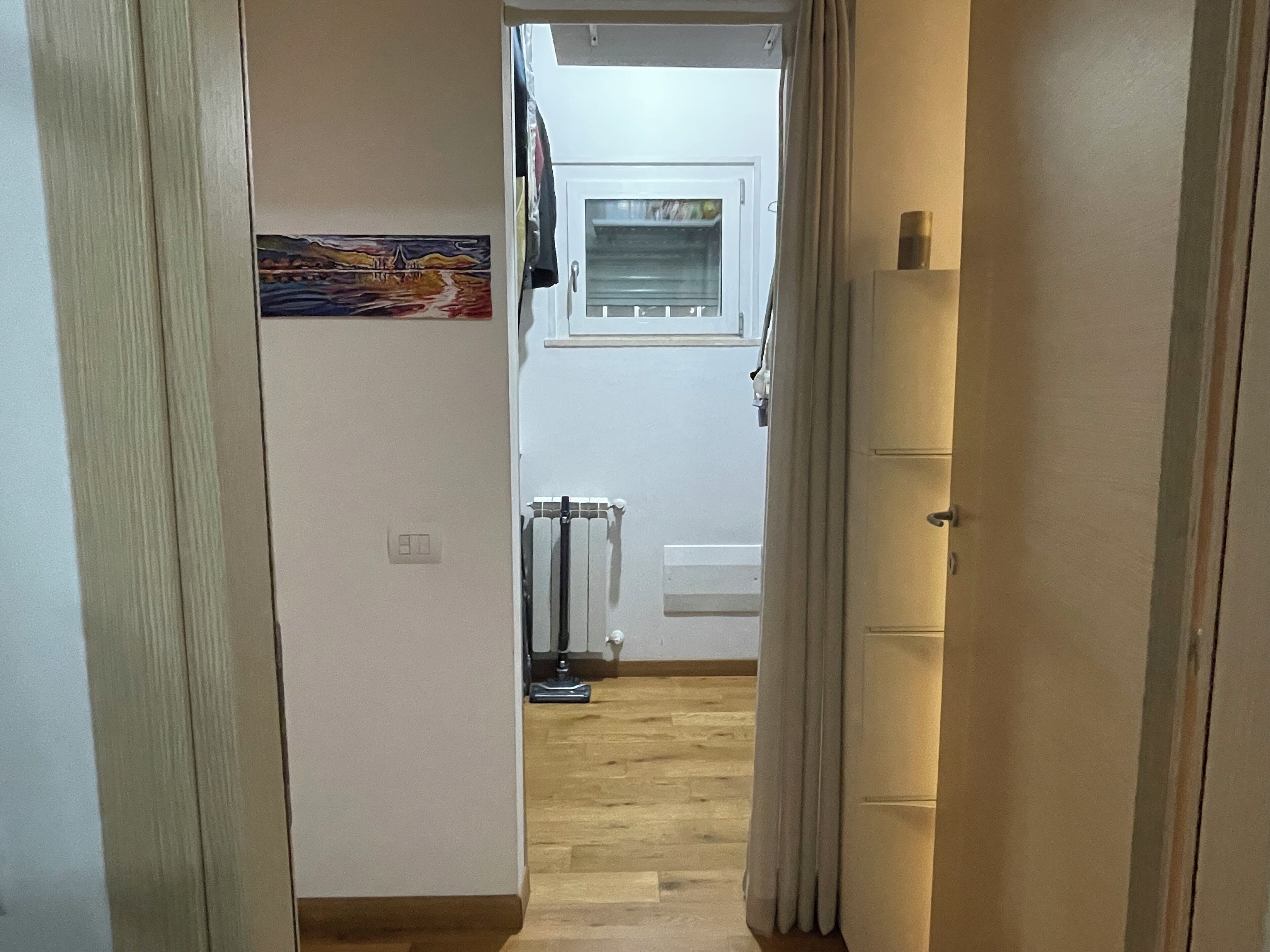 A narrow hallway leading to a kitchen with a radiator, a window, and a door.