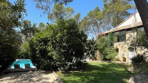 A backyard with a swimming pool, a stone house, and a well-maintained lawn.