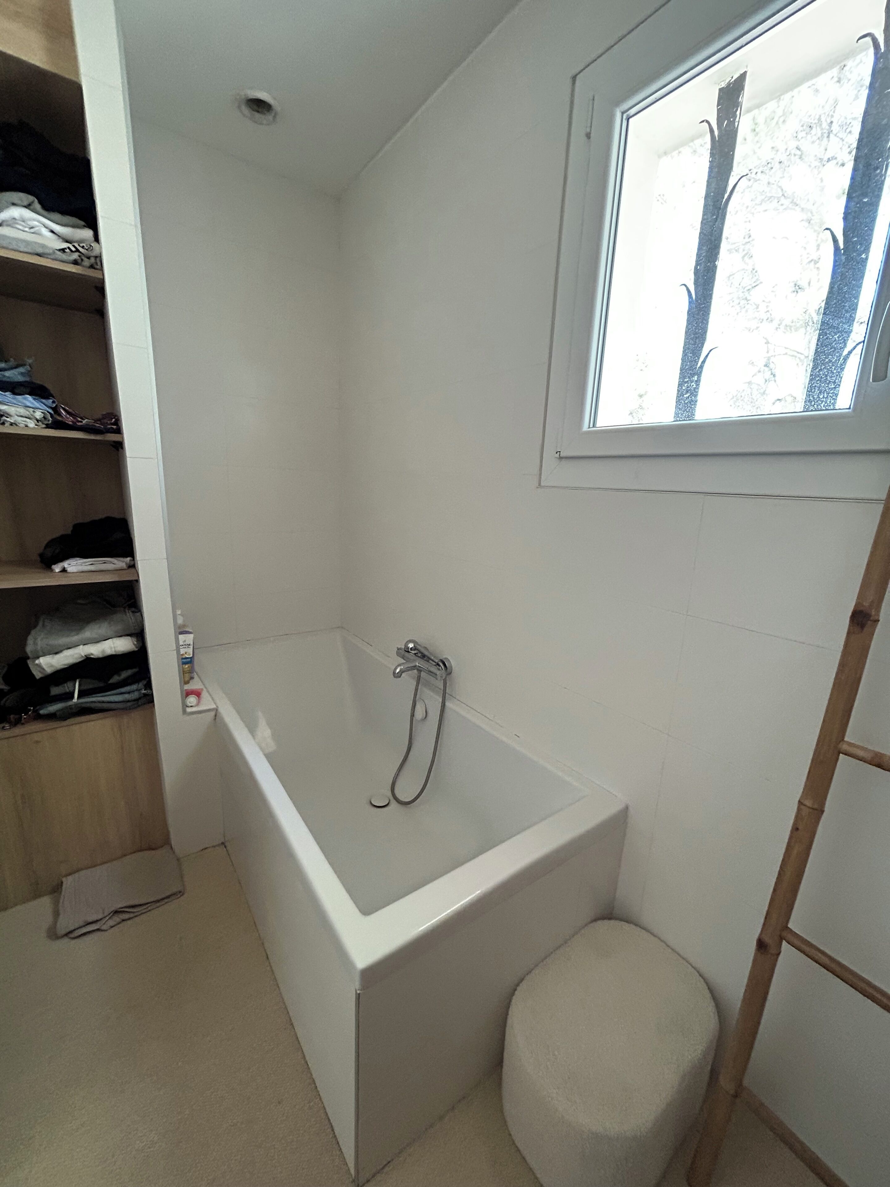 Un bagno piccolo e bianco con una vasca, una finestra e una scala di legno.
