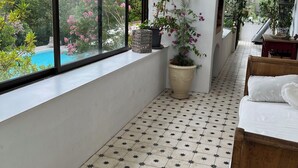 A sunlit room with large windows, a tiled floor, a wooden bench, and potted plants.