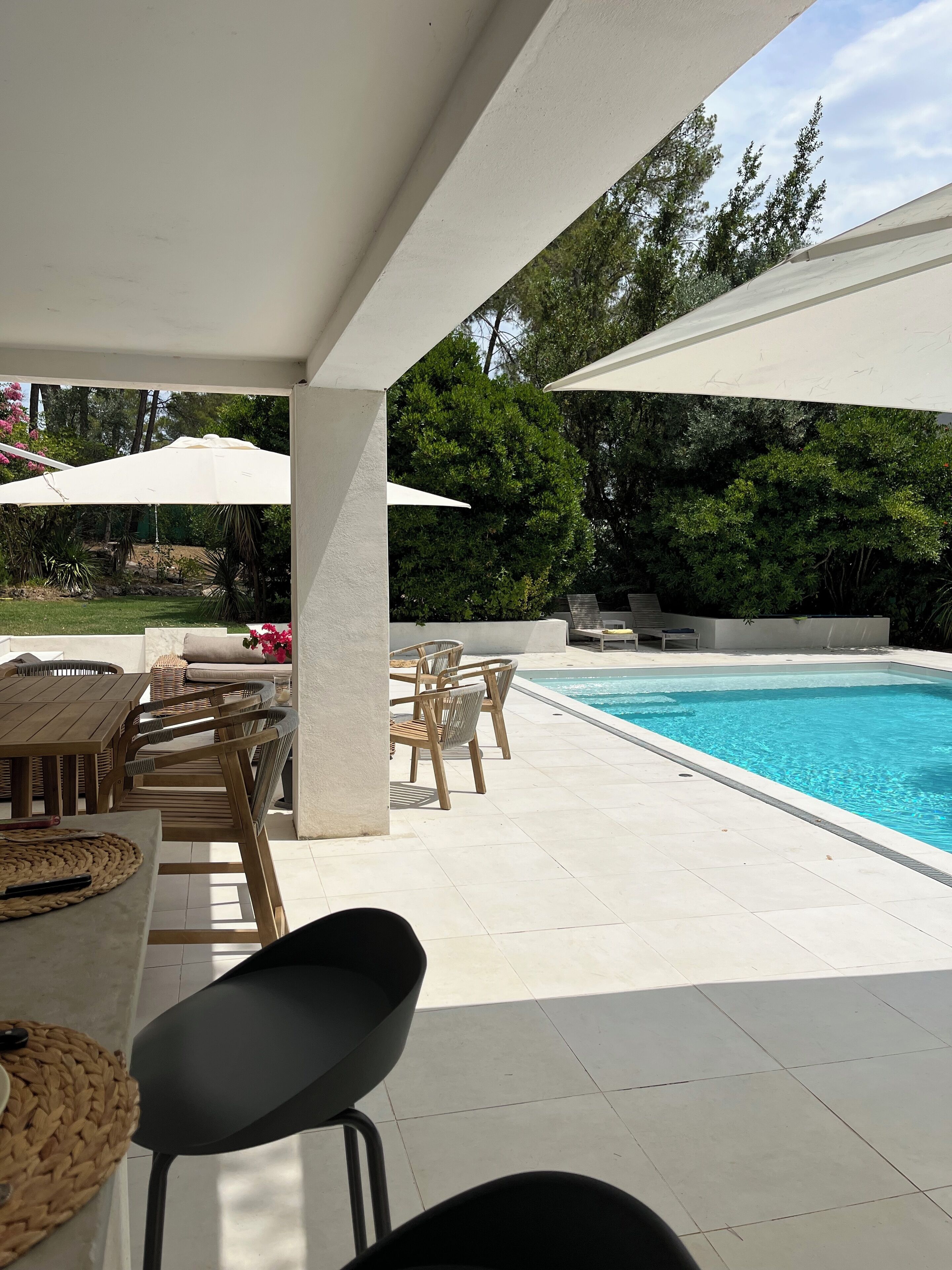 Un espace extérieur avec une piscine, une table et des chaises, entouré de parasols et de verdure.