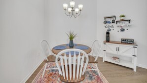 Een eetgedeelte met een ronde tafel, witte stoelen, een kroonluchter, een koffiehoek en een wand met decoraties met koffie thema's.