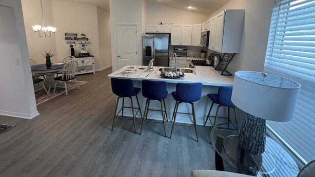 Een moderne keuken met witte kasten, een centraal eiland met barkrukken, en een eethoek met een kroonluchter.