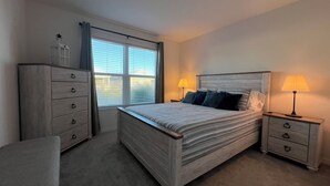 Een slaapkamer met een bed, twee nachtkastjes, een dressoir, een stoel en een raam met zonwering.
