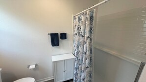 Een badkamer met een toilet, een wastafel met kastjes, en een douchegordijn met een bladmotief.