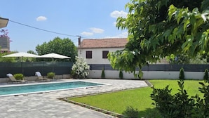 Ein Garten mit Swimmingpool, gepflasterter Terrasse und Rasenfläche.