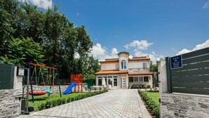 Ein Spielplatz mit Schaukeln und Rutschen, ein gepflasterter Weg und ein Gebäude mit einem Balkon.