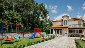Ein Spielplatz mit Schaukeln und Rutschen, ein gepflasterter Weg und ein zweistöckiges Gebäude mit einem Balkon.