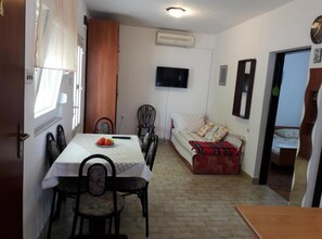 A compact living space with a dining table, chairs, a sofa, and a television mounted on the wall.