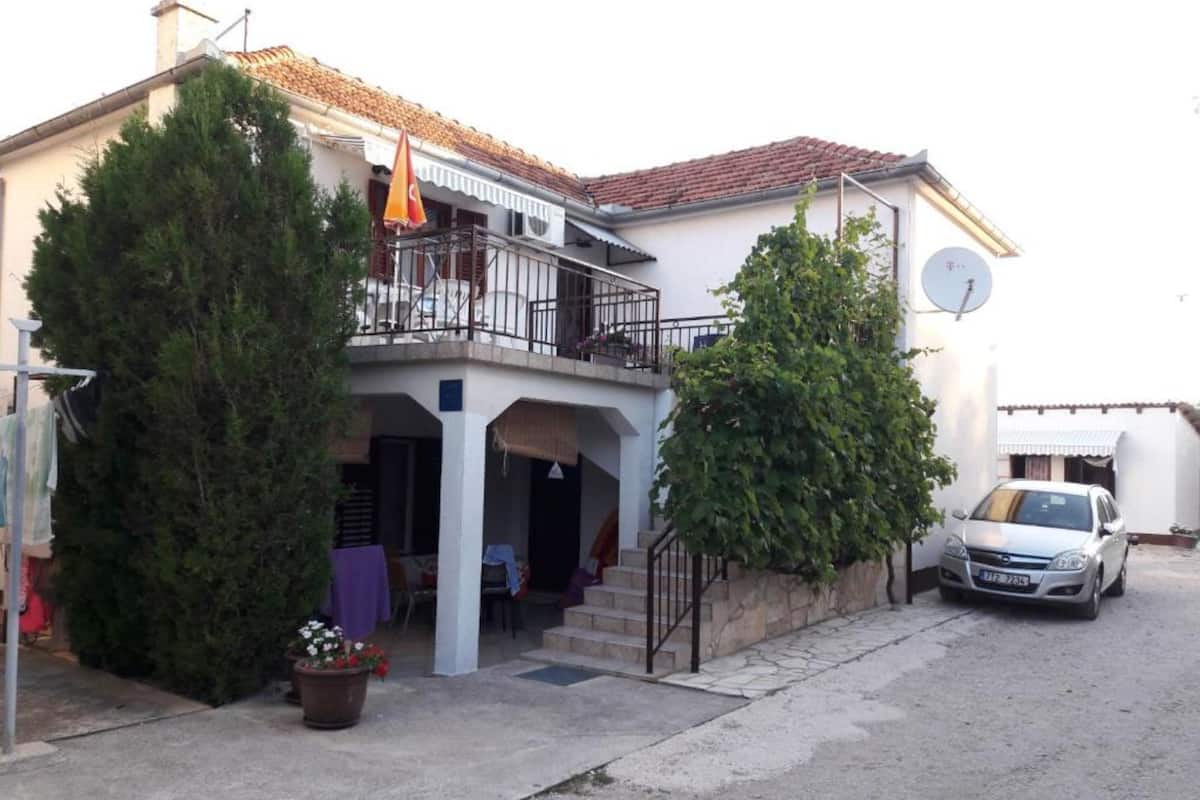 A two-story house with a balcony, a satellite dish, and a parked car.