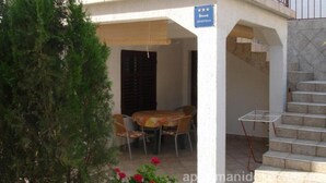 A building with a balcony, a sign indicating it is an apartment, a covered outdoor seating area with a table and chairs, and a staircase leading to an upper level. - Charming Apartments Dokoza Drage (Pakostane)