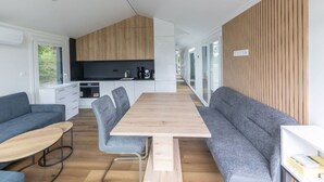 Een moderne keuken met houten kasten, een eethoek met een houten tafel en grijs gestoffeerde zitplaatsen, en een groot raam dat natuurlijk licht binnenlaat.