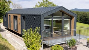 Een modern, gelijkvloers huis met een donker dak, grote glasramen en een balkon.