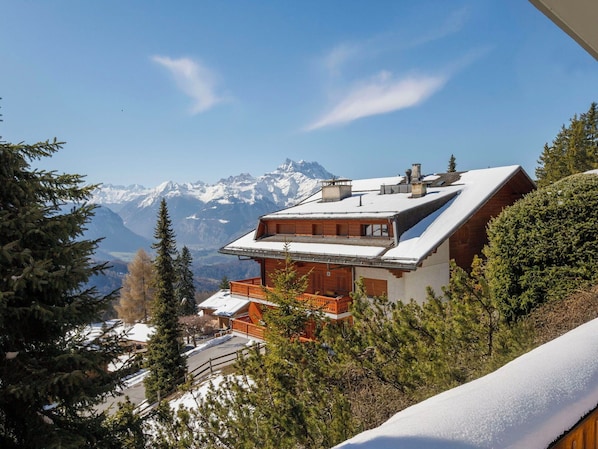 A mountain lodge with a sloped roof, wooden exterior, and a view of snow-capped mountains.