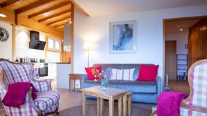 Un salon chaleureux avec un fauteuil à motifs à carreaux, un canapé agrémenté de coussins rouges et blancs, et une table basse en bois sur laquelle est posé un vase.