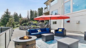 An outdoor patio with a fire pit, blue sofas, and a red umbrella. - Family Retreat -Mt Rainier Views • Pool • Hot Tub • Sleeps 11 (Auburn)