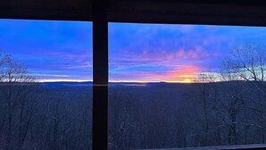 Uitzicht vanuit een raam op een bebost landschap in de zonsondergang.