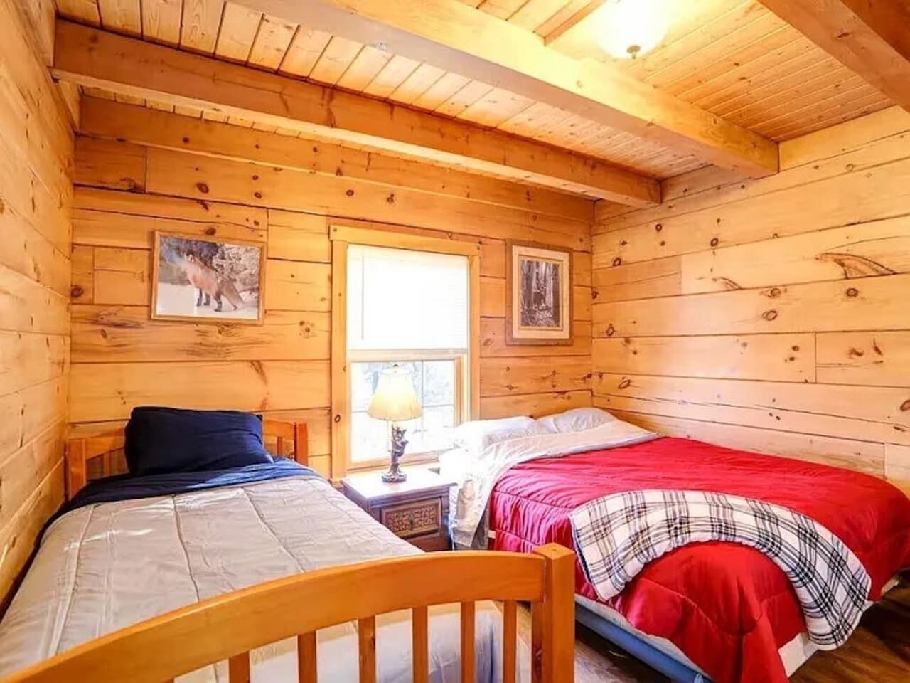 Una cabaña con dos camas de madera, una ventana y una lámpara.