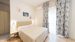Un dormitorio con cama, mesita de noche, decoración en la pared y una ventana con cortinas florales.