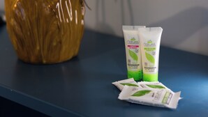 Una encimera de baño con dos botellas de champú y gel de ducha Naturel, y una planta en maceta.