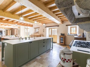 Una cocina amplia con una isla grande, vigas de madera y una pared de acento de piedra.