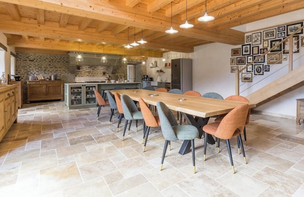 Una cocina moderna con pared de piedra, vigas de techo de madera y un comedor con una mesa larga y sillas.