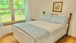 A bedroom with a bed, wooden headboard, a window with a view of greenery, and a framed picture on the wall. - Lydia's Lodge in Pelham (Pelham)