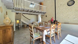 A dining area with a wooden table and chairs, a staircase, and a rustic stone wall. - Bright cottage with enclosed garden and parking (Comberanche-et-Épeluche)