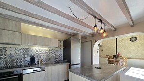 A modern kitchen with a central island, built-in appliances, and patterned backsplash. - Bright cottage with enclosed garden and parking (Comberanche-et-Épeluche)