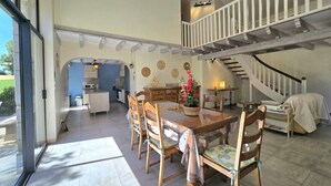 A spacious dining area with a high ceiling, a staircase, and a kitchen in the background. - Bright cottage with enclosed garden and parking (Comberanche-et-Épeluche)