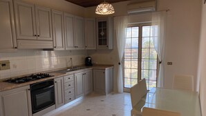 Een keuken met witte kasten, een gasfornuis, een oven, een koffiezetapparaat, en een eethoek met een glazen tafel en stoelen.