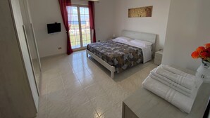 Een slaapkamer met een bed, nachtkastje, televisie, raam met gordijnen en uitzicht op het omliggende landschap.