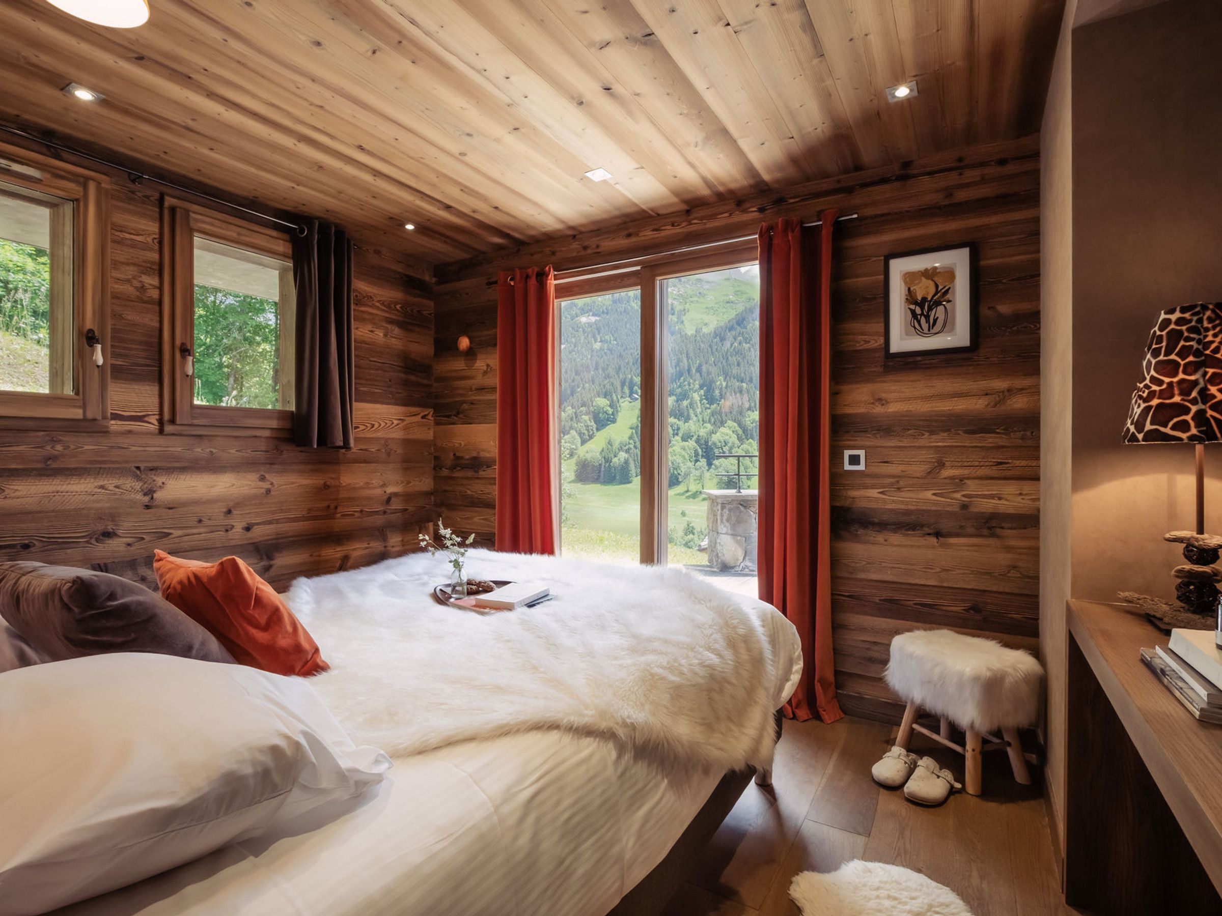 A wooden cabin bedroom with a bed, pillows, a nightstand, and a view of the outdoors.