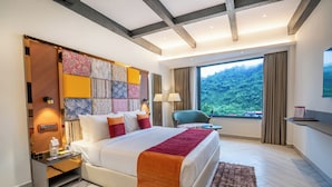 Une chambre d’hôtel moderne dotée d’un grand lit, d’une table de chevet, d’un bureau, d’une chaise et offrant une vue sur une montagne boisée.