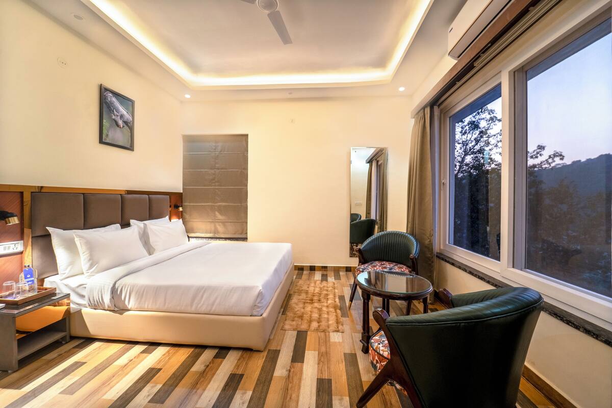 Hotelkamer met een bed, een stoel, een klein tafeltje, een raam met uitzicht en een plafondventilator.