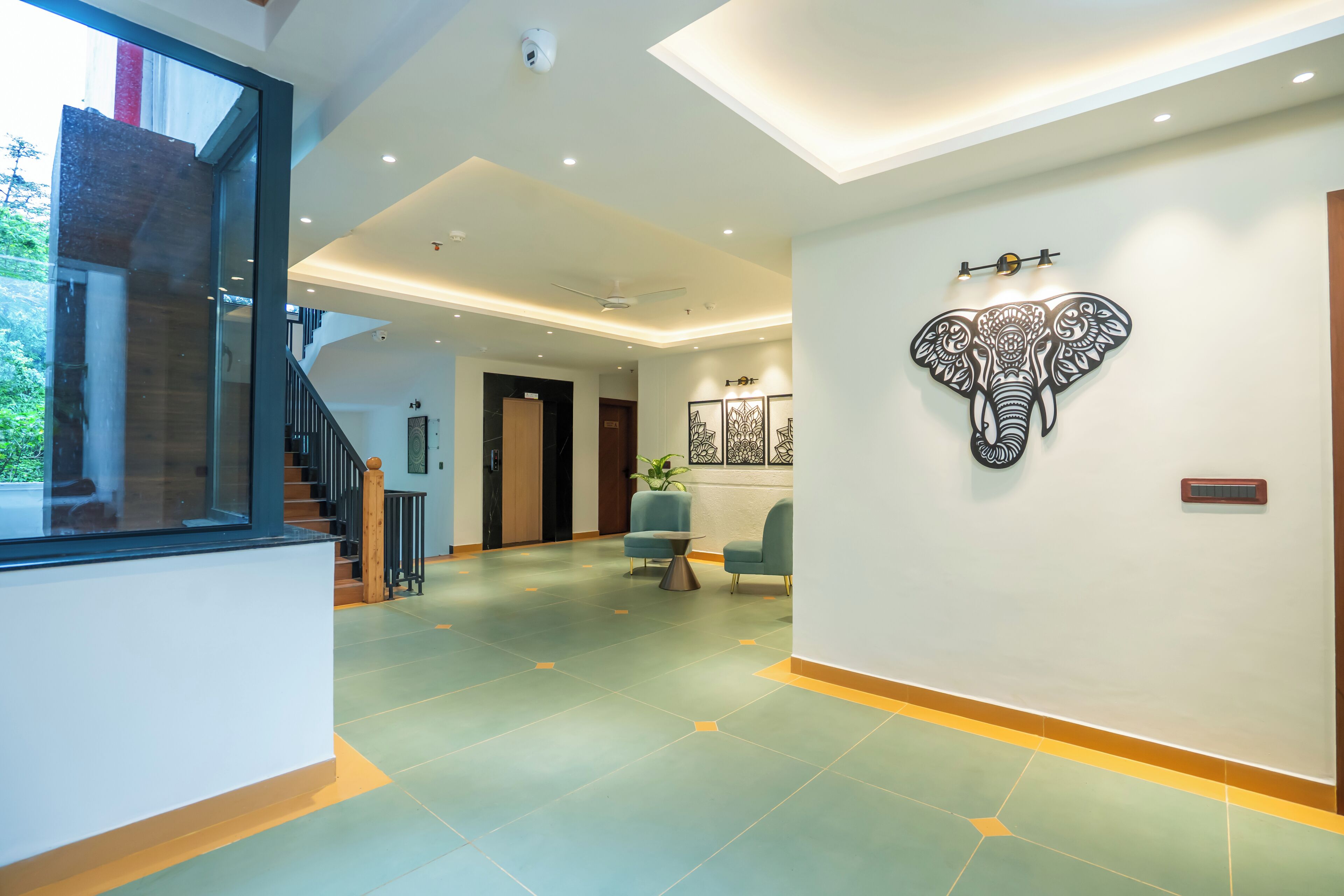 Un moderno vestíbulo de hotel con una escalera, un mostrador de recepción y una obra de arte de un elefante en la pared.