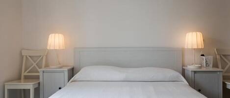 Une chambre d’hôtel avec un grand lit, deux tables de chevet avec des lampes, une chaise et des serviettes soigneusement pliées sur le lit.