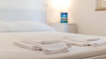 Ein ordentlich bezogenes Bett mit gefalteten Handtüchern und einem Nachttisch mit einer Lampe und einem gerahmten Bild.