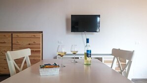 A dining area with a table, chairs, a television mounted on the wall, and two glasses of wine. - LOCANDA SU RECREU (Cala Gonone)