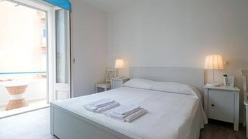 A hotel room with a bed, two bedside tables, a lamp, and a view through a sliding door.