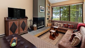 A living room with a flat-screen TV, a fireplace, a sofa, and a large window with a view of trees. - Dobie 36  with Wintergreen Advantage (Wintergreen)