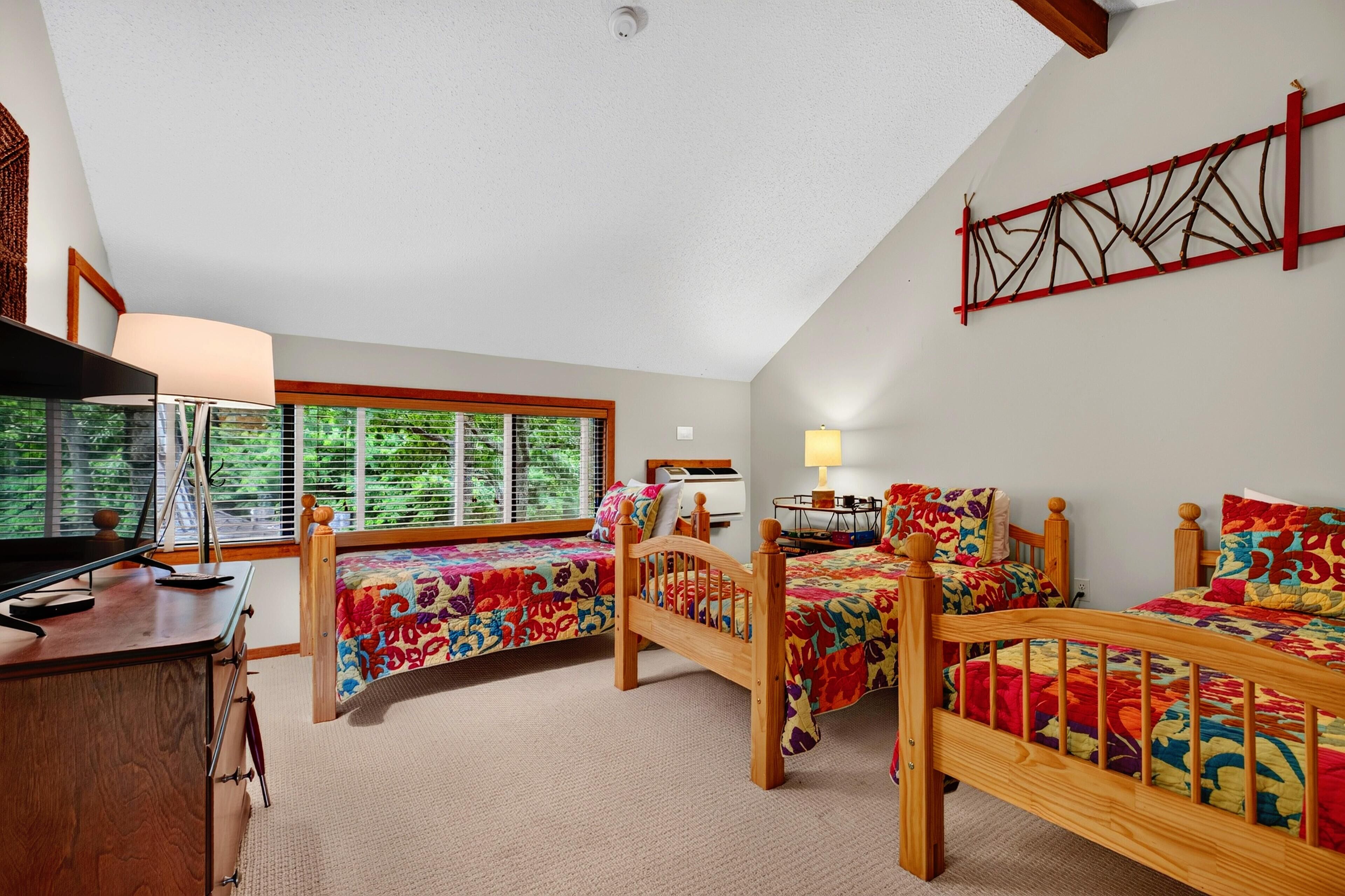 A bedroom with three wooden beds, a desk, and a window with blinds.