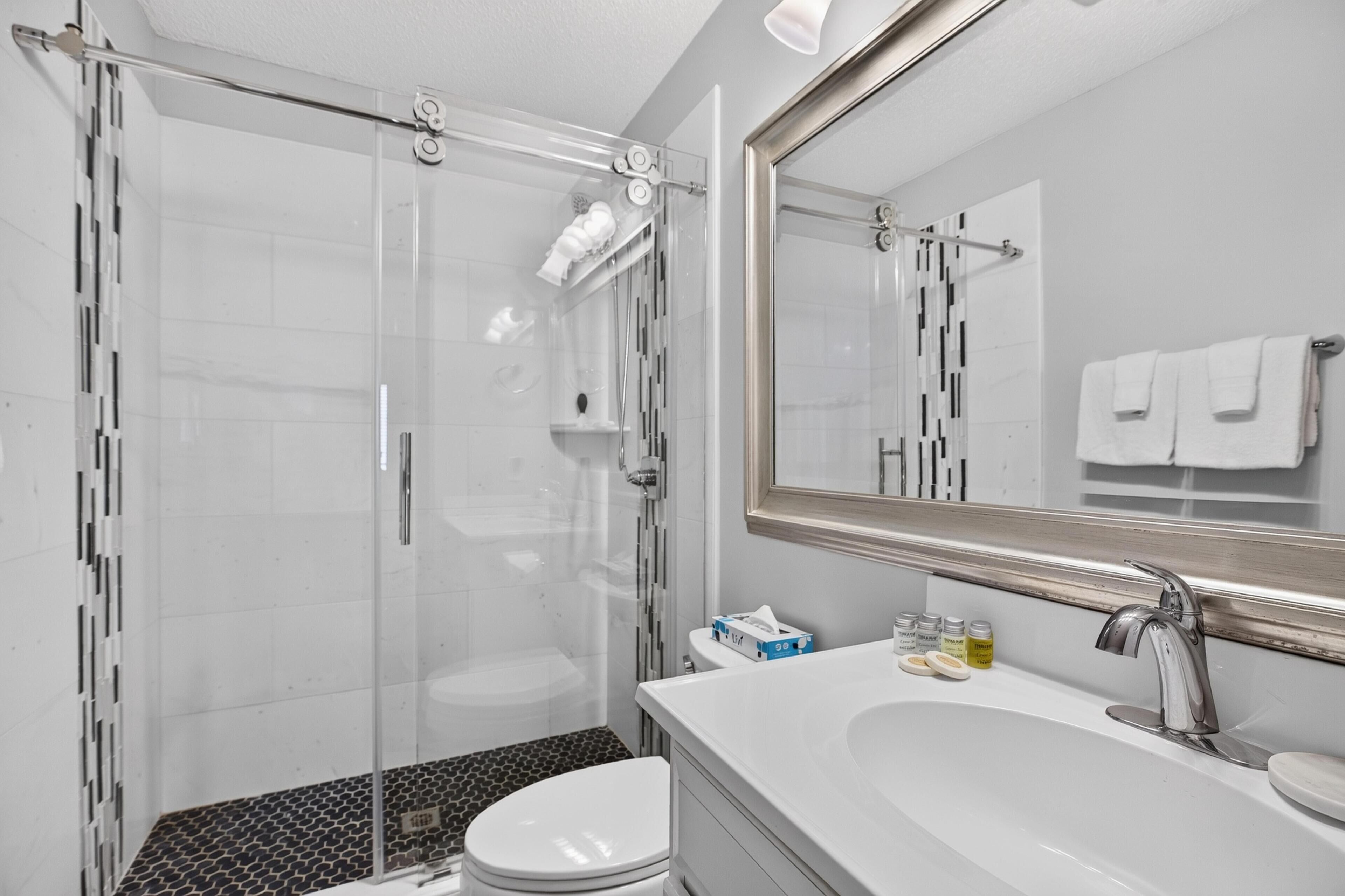 Ein modernes Badezimmer mit Duschkabine aus Glas, einem weißen Waschbecken mit großem Spiegel und einer Toilette.