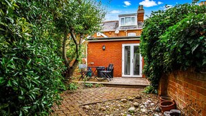 Una casa de ladrillo con un patio, una puerta y un pequeño jardín con plantas en macetas.