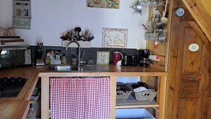 A rustic kitchen with wooden beams, a sink, a stove, and various kitchen utensils. - House for rent by the river in a peaceful hamlet (Saint-Cirgues)