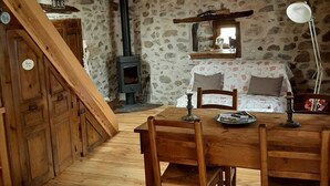 A cozy room with a wooden dining table, chairs, a sofa, and a stone wall. - House for rent by the river in a peaceful hamlet (Saint-Cirgues)