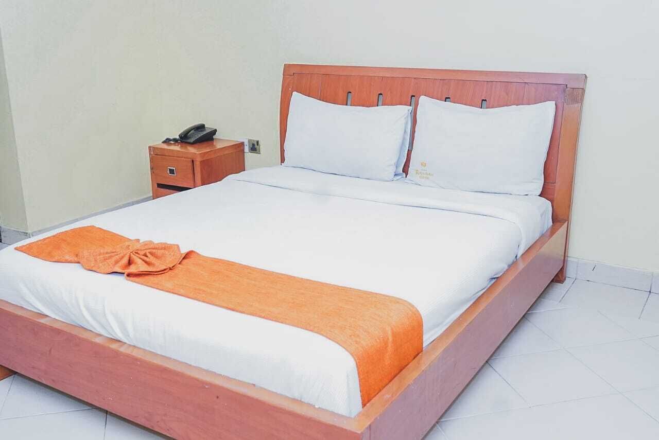 A standard hotel room with a wooden bed frame, white bedding, and a single bedside table with a telephone.