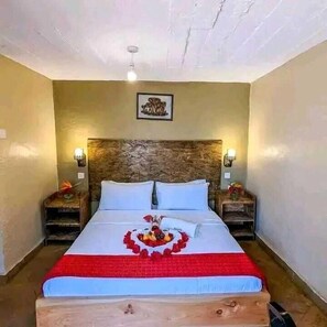 A hotel room with a large bed, wooden headboard, two bedside tables with lamps, and a framed picture on the wall. - Raya Hotel CBD (Nairobi)