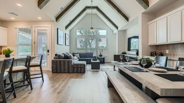 A spacious living area with a high ceiling, a kitchen with white cabinets, and a dining area with a long table and chairs.